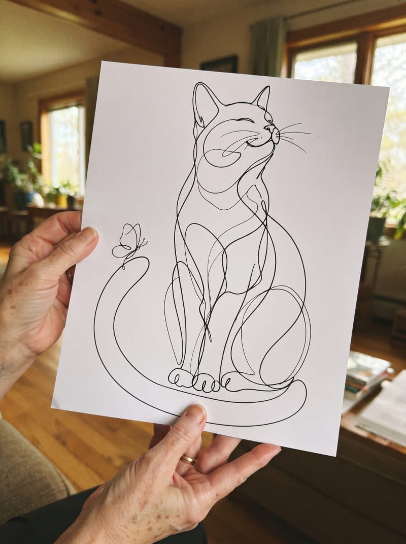 Her own hands holding up the finished one-line cat she just drew