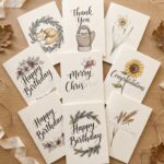 Nine finished hand drawn cards fanned on a table showing Happy Birthday, Thank You, Merry Christmas and Congratulations across all four seasons, each phrase half inked and half dotted to trace