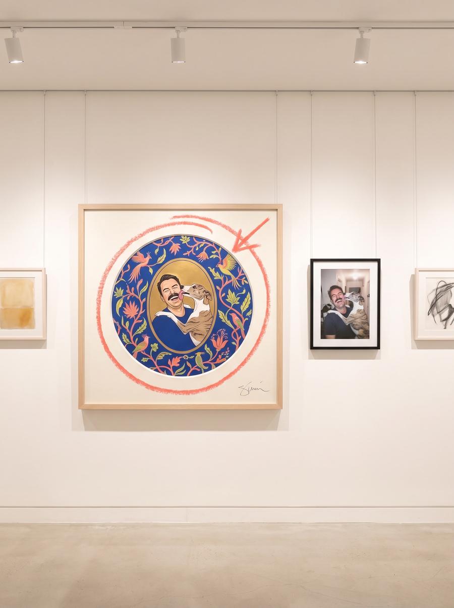 A gallery wall hung with a large signed roundel of a man being licked by his dog, the original phone snapshot framed small beside it