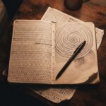 An open notebook on a bedside table covered in repeated ballpoint dashes, scallops and one long spiral
