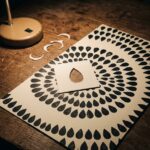 One hand-cut petal stencil on a night worktable, the same petal stamped over and over into rings and a border