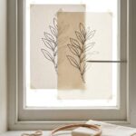 Hand embroidery patterns for beginners traced at a window: a printed botanical outline taped to the glass with cotton over it, the line glowing through