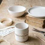 Paint your own pottery ideas planned at home: bisque mug, bowl and plate with a paper design strip wrapped round the mug