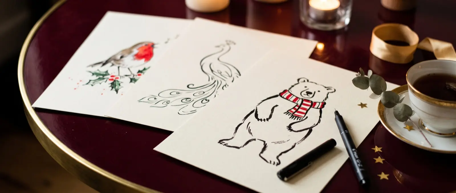 Robin, peacock and bear pages fanned on a lacquer table with tea